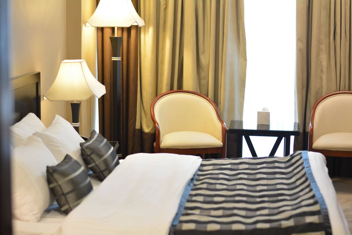 A hotel room with a bed, two chairs, a small table, and a lamp.