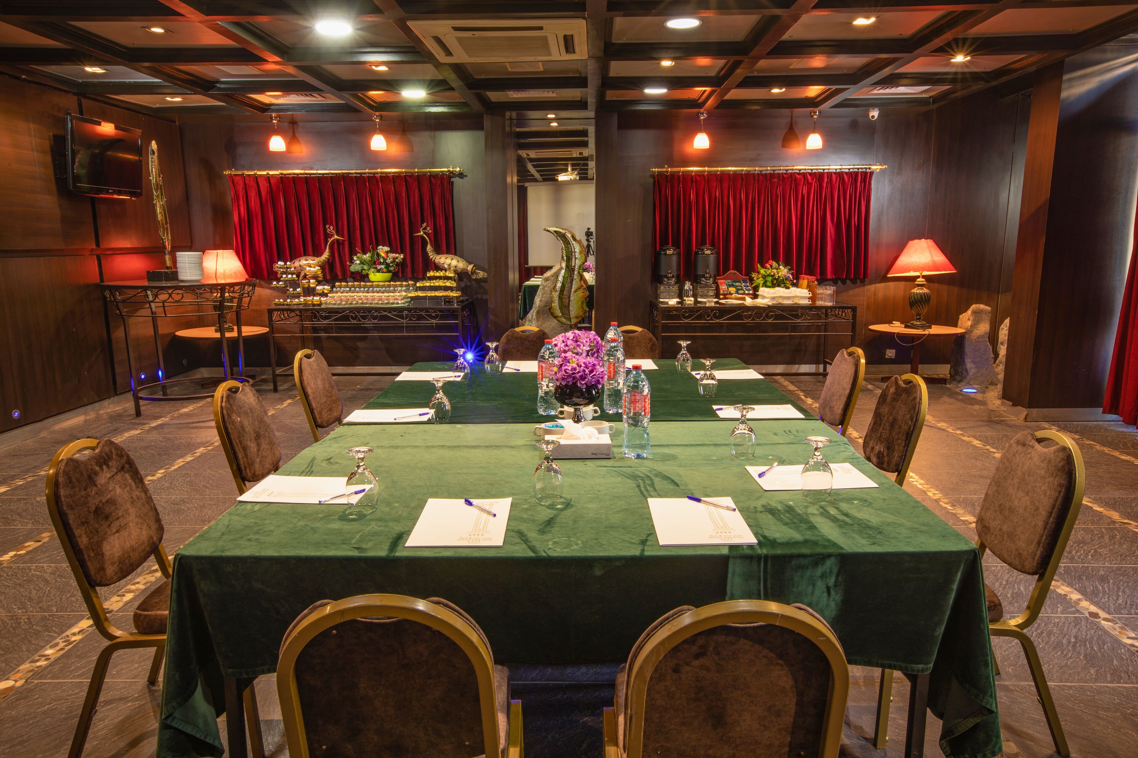 Uma sala de conferências com uma mesa comprida, cadeiras e um palco com cortinas.