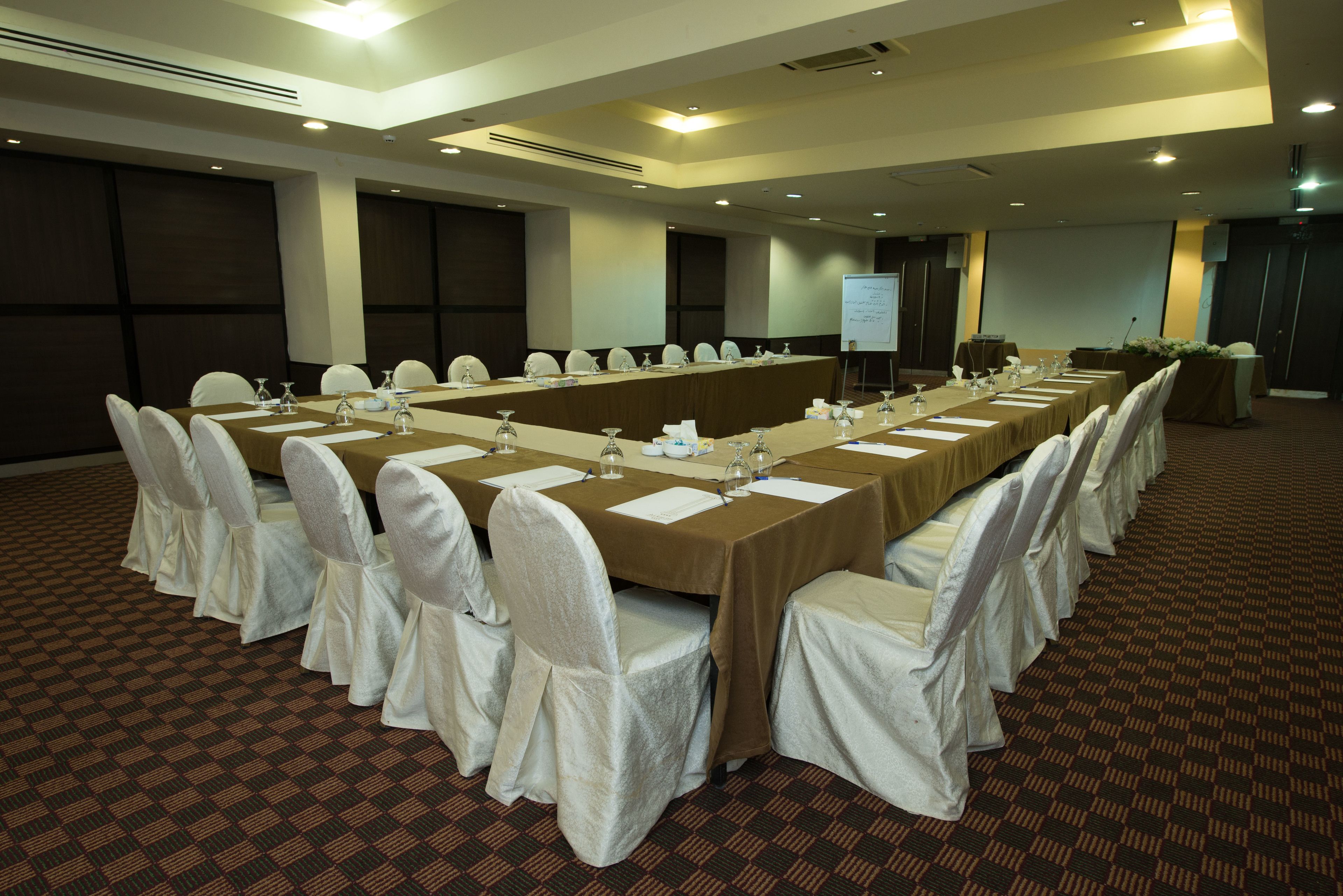 A conference room with a long table, white chairs, and a projector screen.