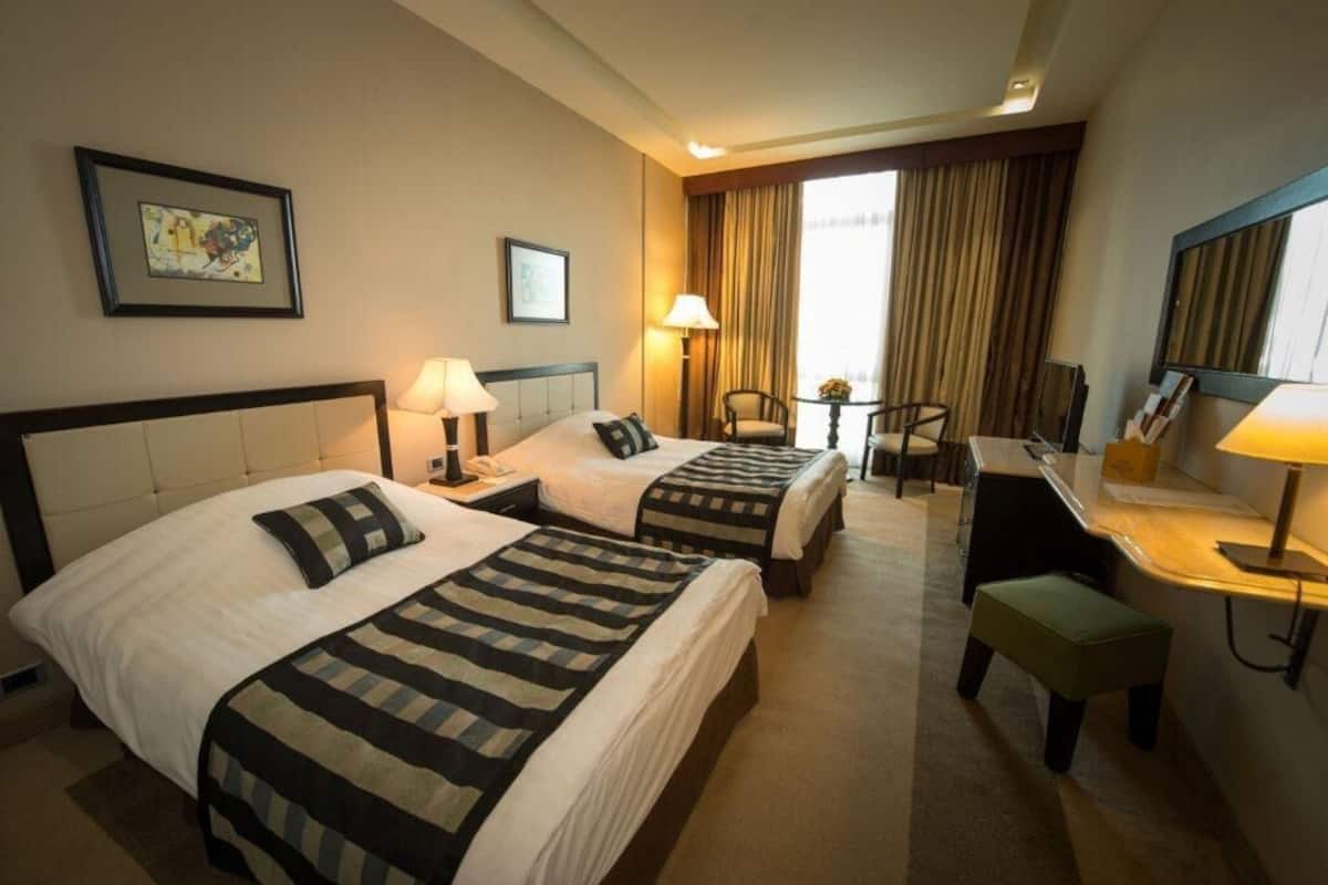 A hotel room with two beds, a desk, a chair, and a small table.