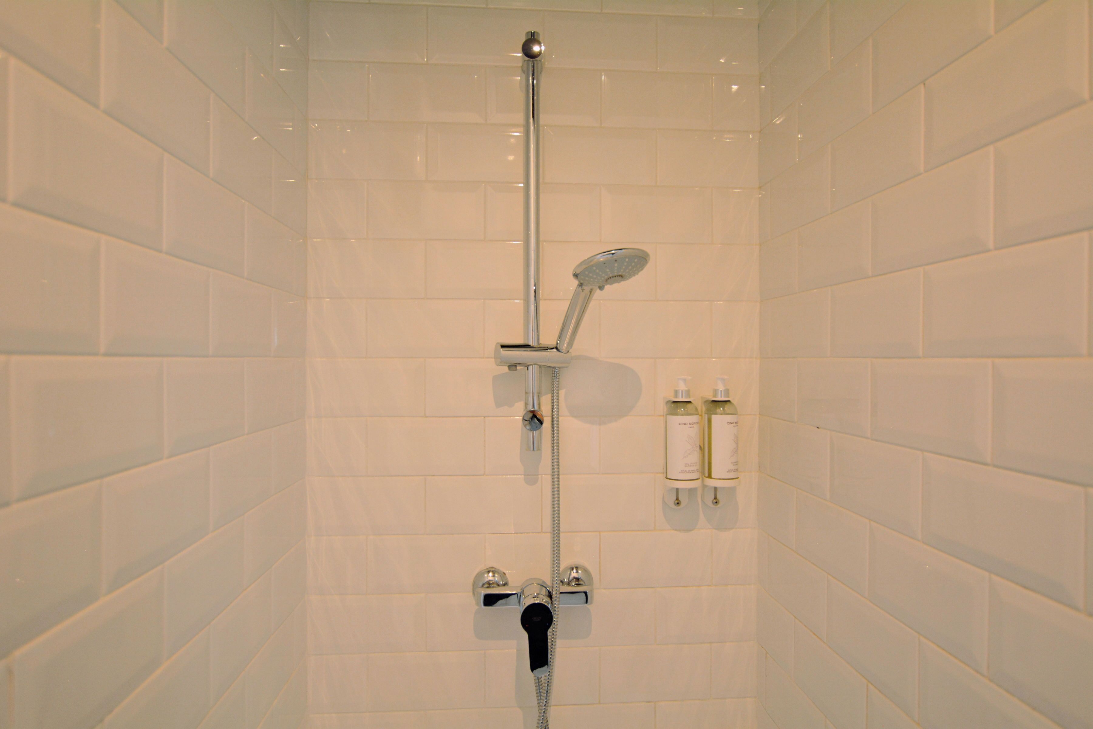 Ducha con cabezal de ducha de mano, grifo empotrado en la pared y dos botellas de artículos de aseo colgadas.