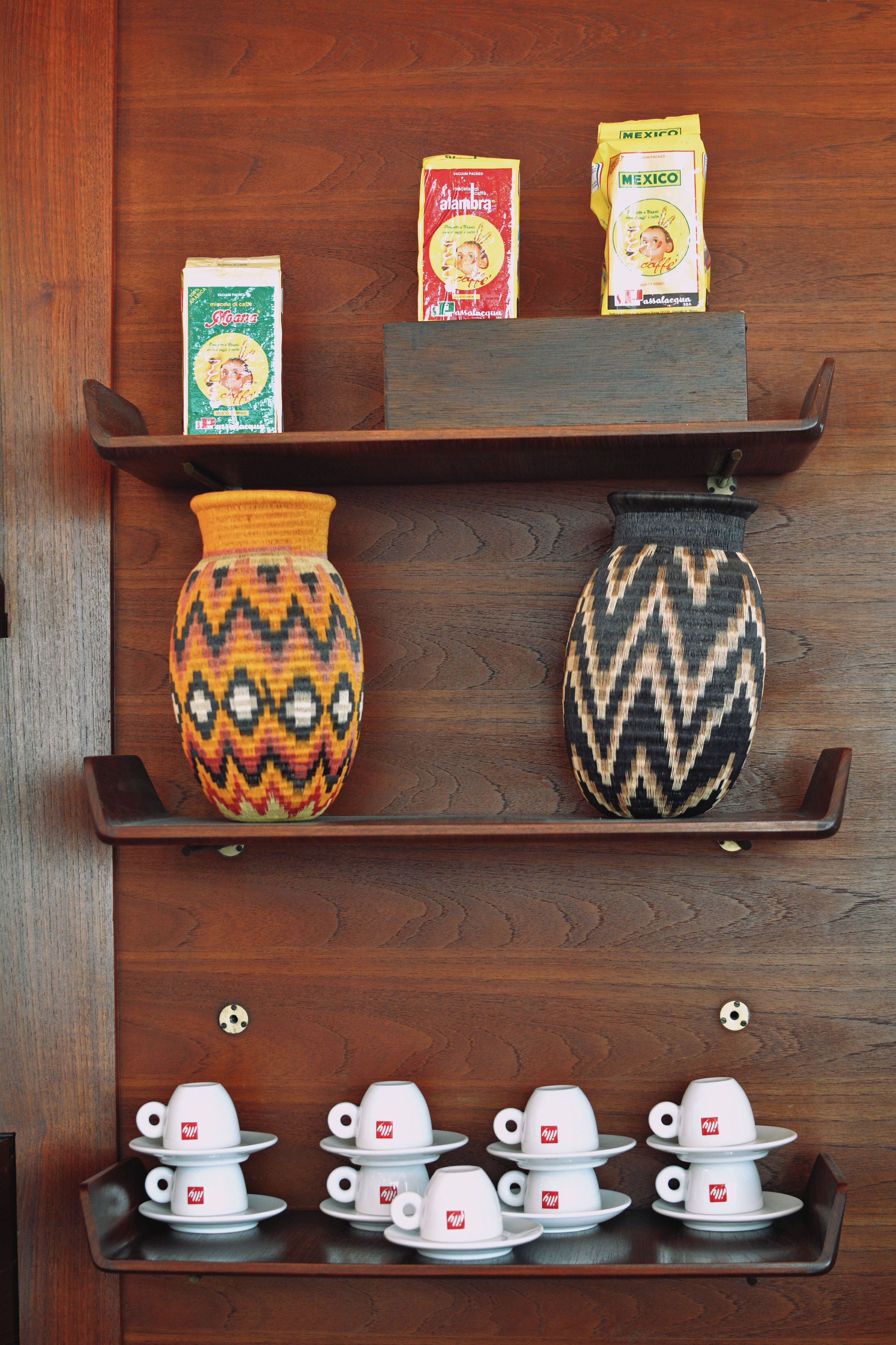 Una estantería de madera con un jarrón decorativo, dos cajas de café instantáneo y una bandeja con tazas de té.