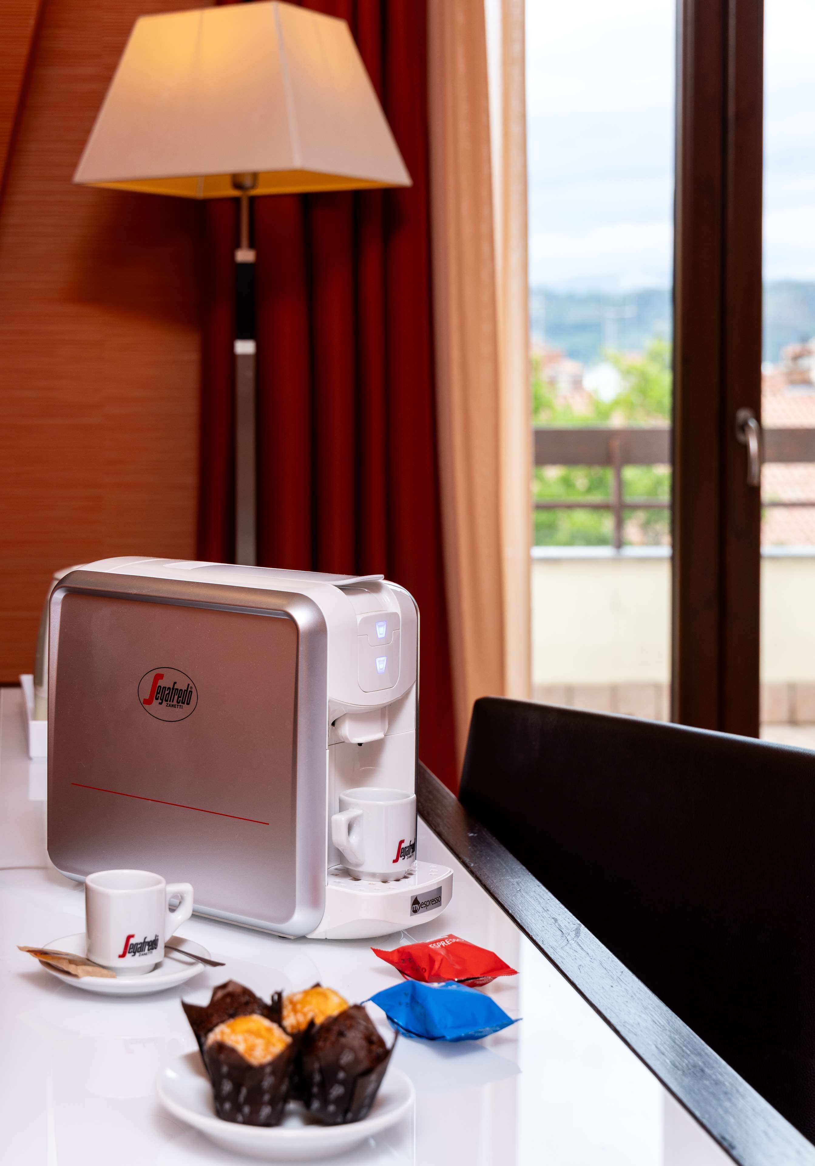 A hotel room with a coffee machine, a cup, and a plate of muffins.