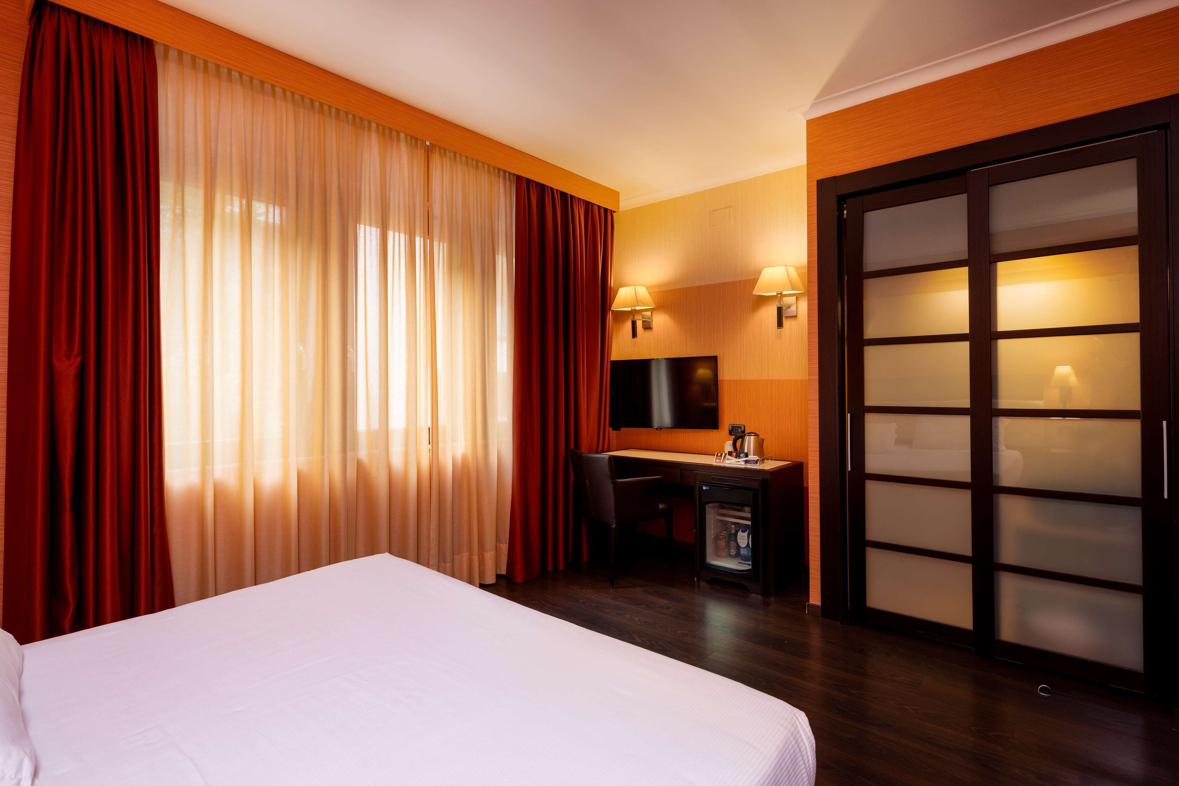 A hotel room with a bed, a desk, a chair, a television, and a sliding door.