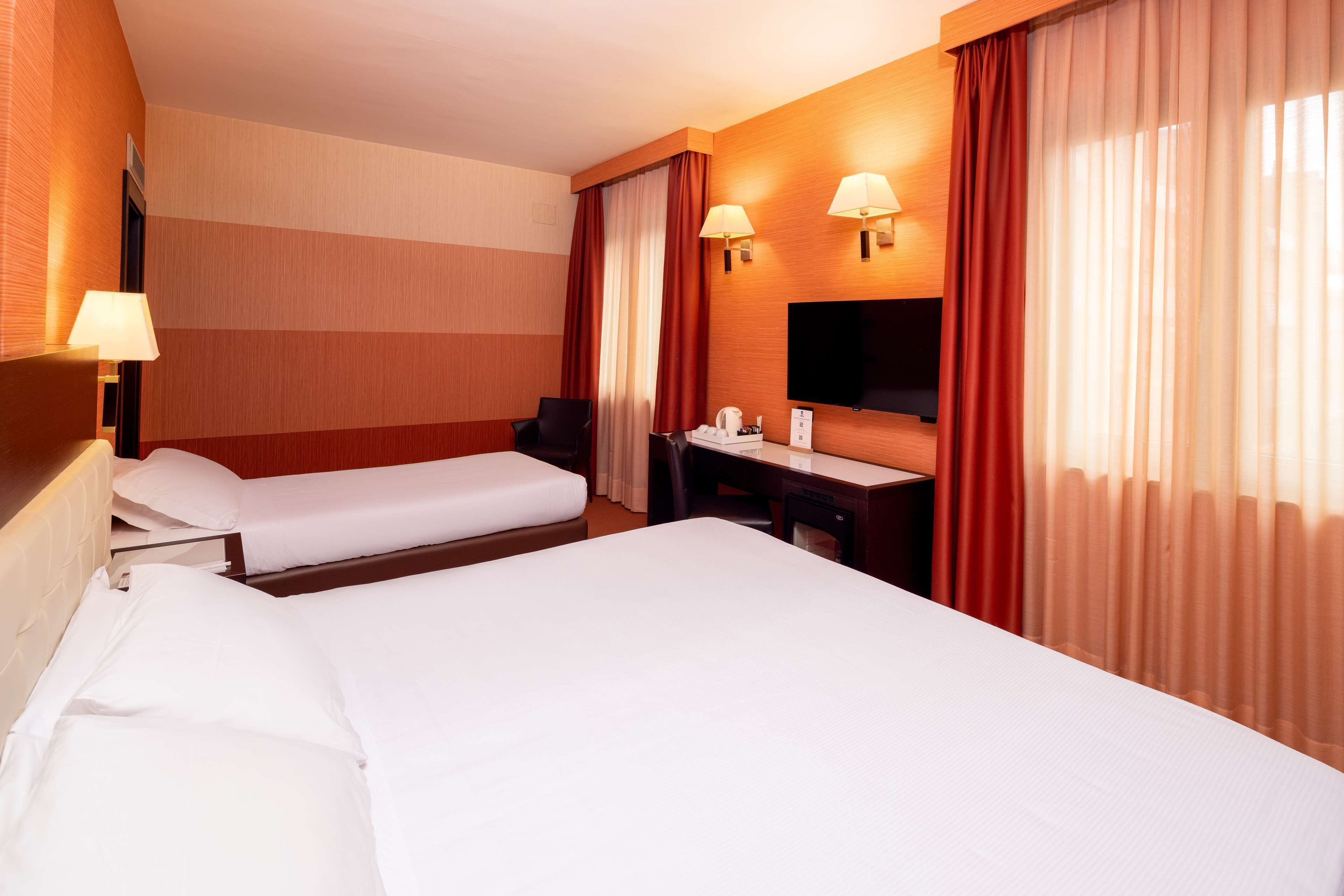 Habitación de hotel con dos camas, un escritorio, una silla, un televisor y dos lámparas de pared.