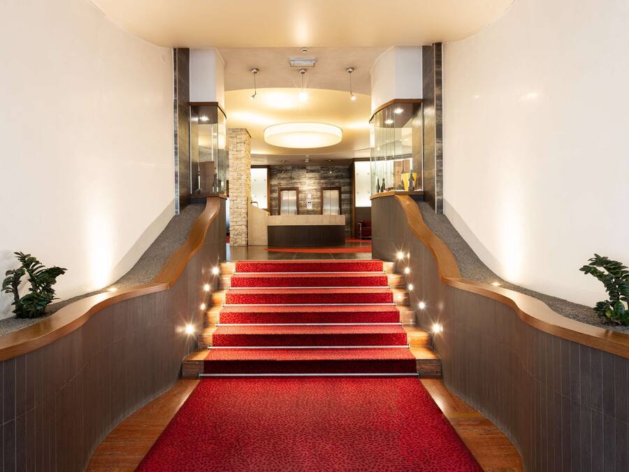 Un moderno vestíbulo de hotel con una imponente escalera, un mostrador de recepción y una zona de recepción.
