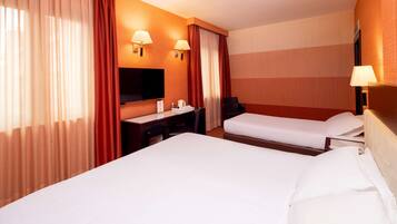 Une chambre d’hôtel avec deux lits, un bureau, une chaise, un téléviseur et deux lampes fixées au mur.