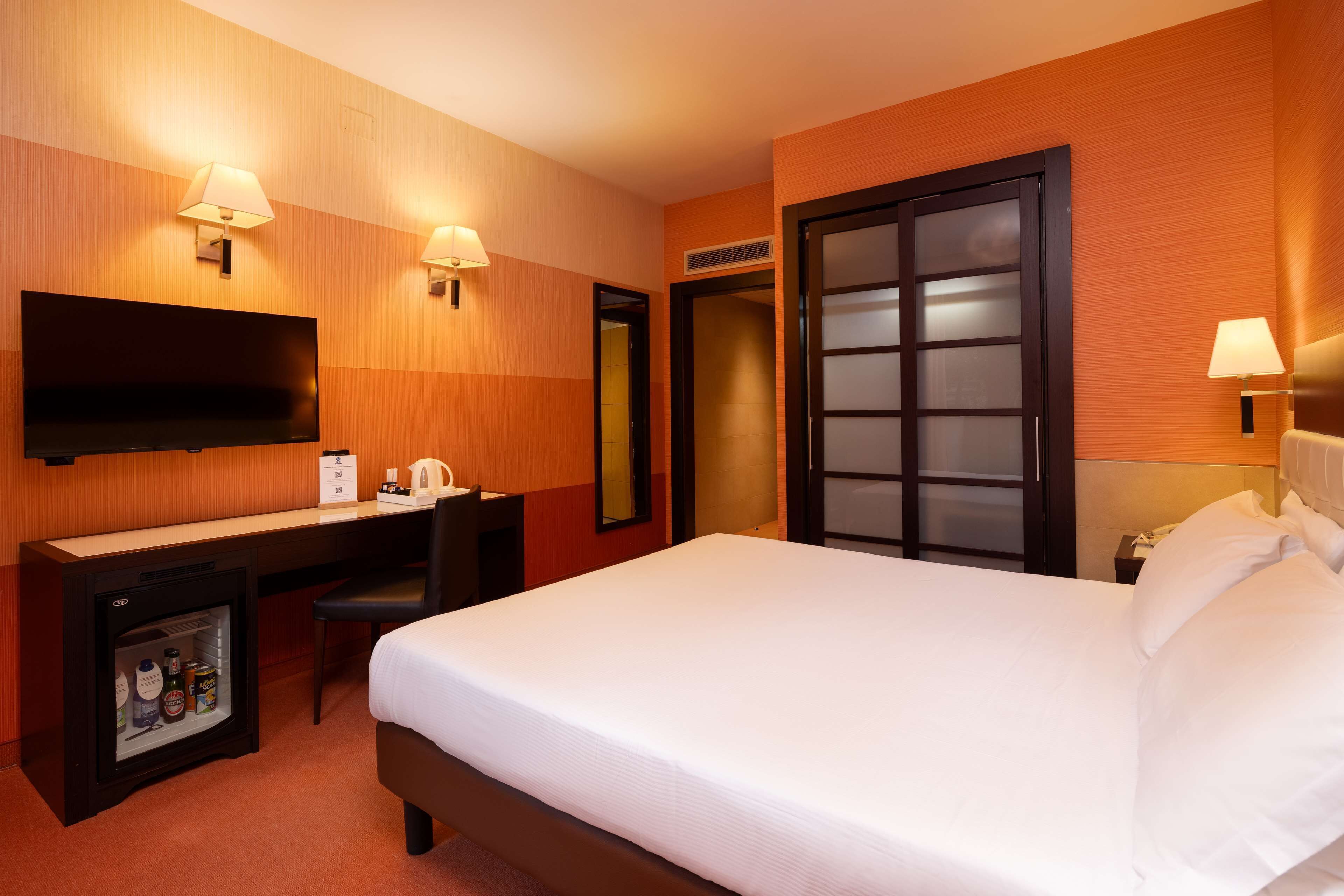Une chambre d’hôtel comprenant un lit, un bureau avec un téléviseur à écran plat, un minibar et deux lampes fixées au mur.