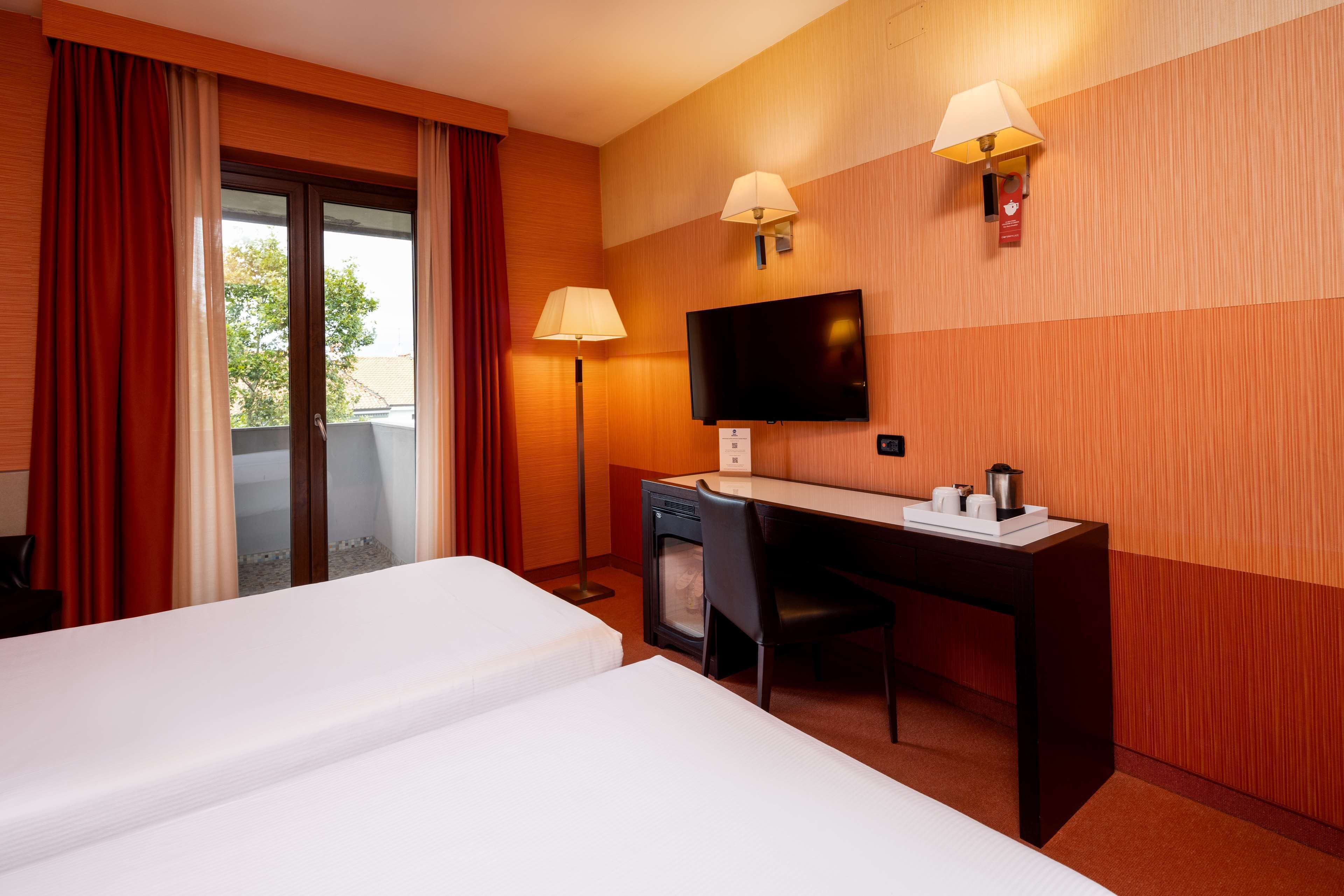 A hotel room with two beds, a desk, a chair, a television, and two wall lamps.