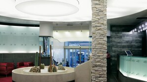 Un moderno vestíbulo con un mostrador de recepción central, una columna de piedra y una partición de vidrio.