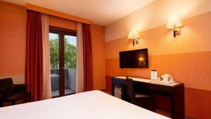 Habitación de hotel con cama, escritorio, silla, televisión y puerta corrediza al exterior.