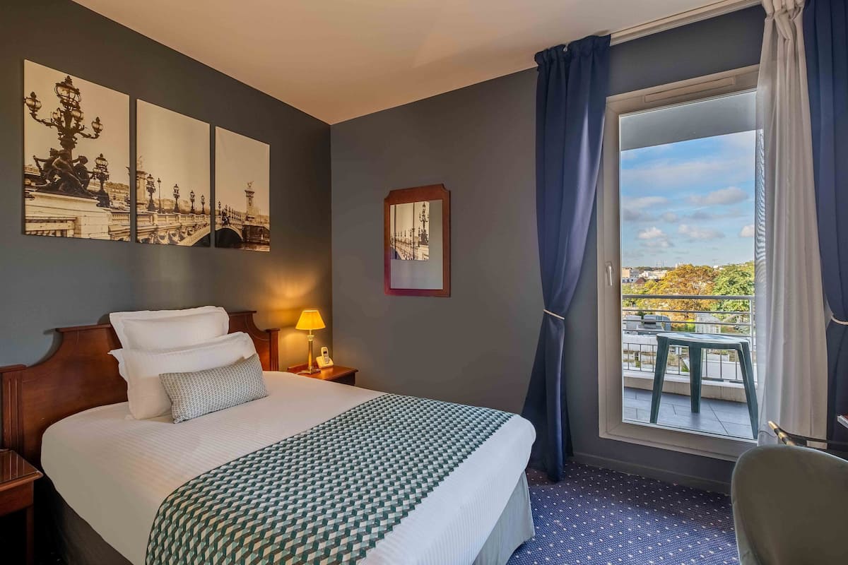 A hotel room with a large bed, a view of a balcony, and a painting on the wall.