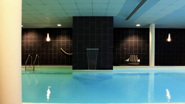 A swimming pool with a black tiled wall, a ship decoration, and a water fountain. - Amiral Hôtel (Paris)