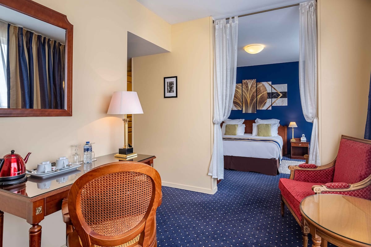 A hotel room with a bed, a desk with a lamp, a chair, and a dining table.