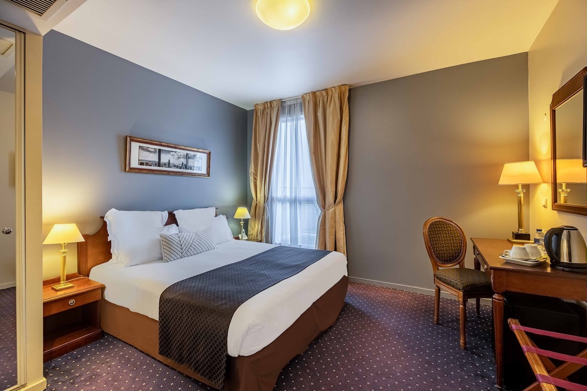 A hotel room with a large bed, a desk with a chair, a lamp, and a picture on the wall.