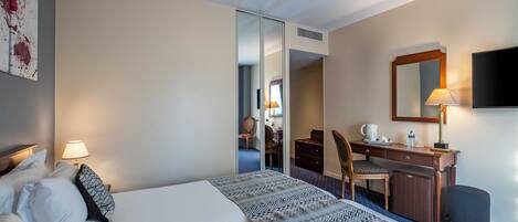 A hotel room with a bed, desk, chair, and a television.