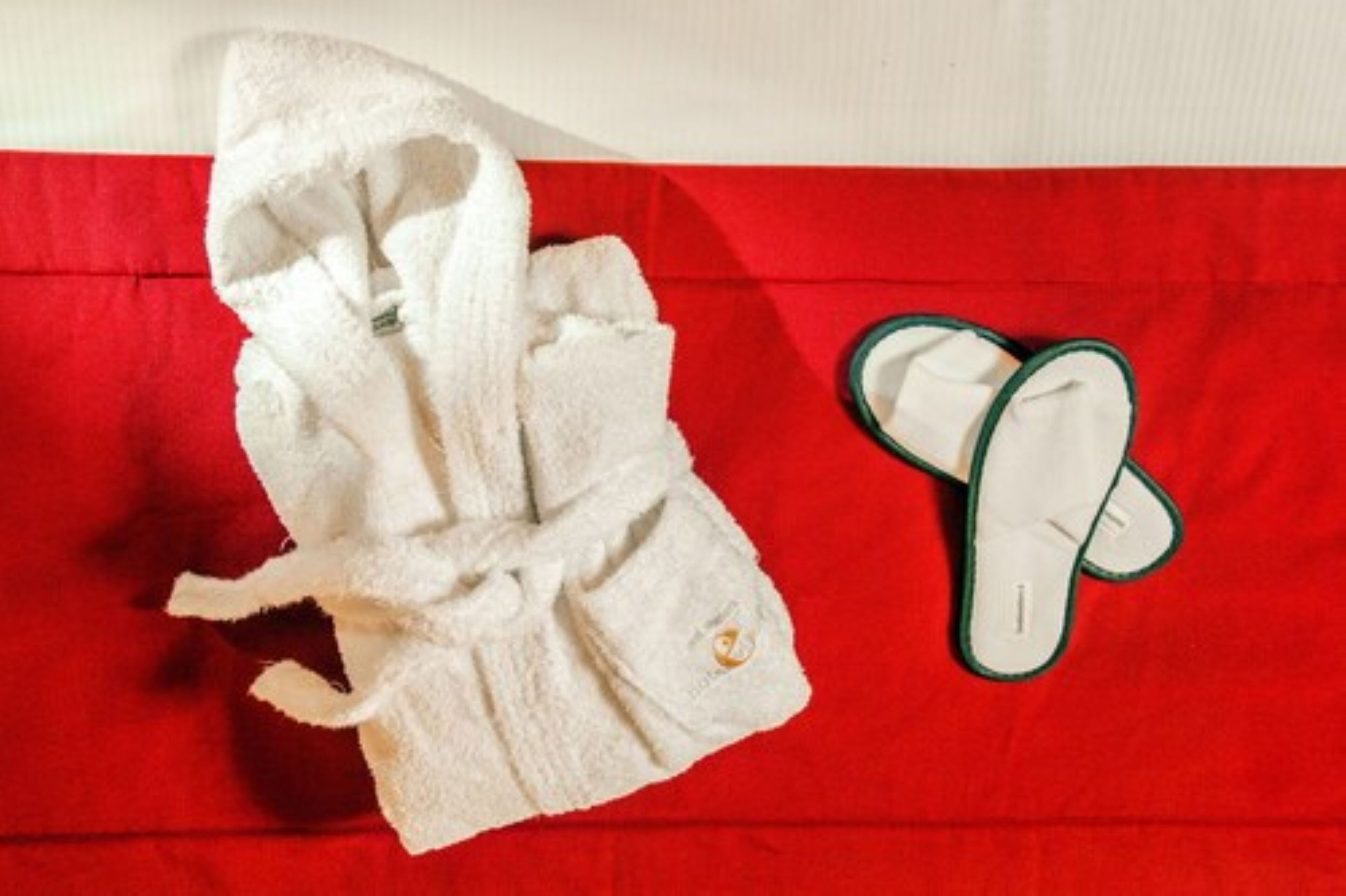 A white bathrobe and a pair of slippers on a red surface.