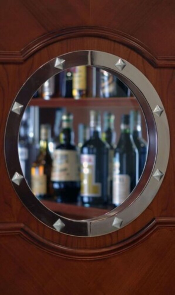 A circular mirror with a metallic frame, reflecting a blurred interior scene with shelves of bottles.