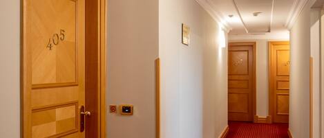 Pasillo de hotel con puertas de madera con los números 405 y 407, una alfombra roja y una pared blanca con una placa pequeña.