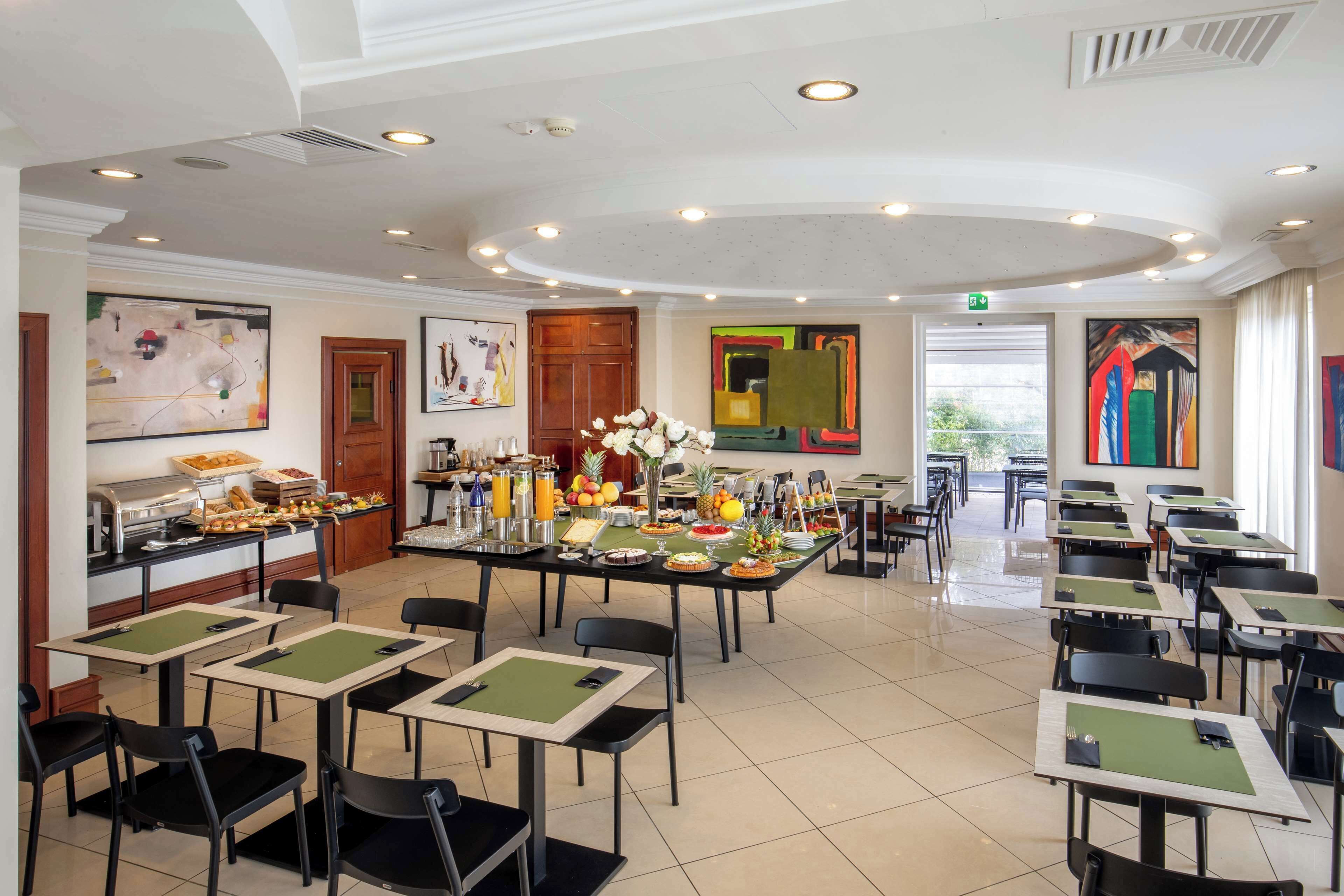 A dining area with tables and chairs, a buffet with various food items, and artwork on the walls.