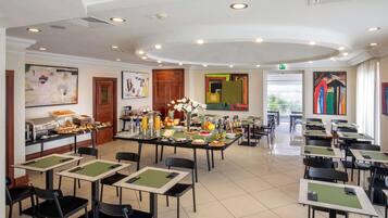 Un espace repas avec des tables et des chaises, un buffet proposant divers plats, et des œuvres d’art accrochées aux murs.