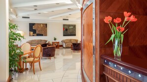 Un hall d’entrée spacieux, avec un comptoir de réception en bois, un vase rempli de fleurs rouges et un coin salon agrémenté de canapés et de fauteuils.