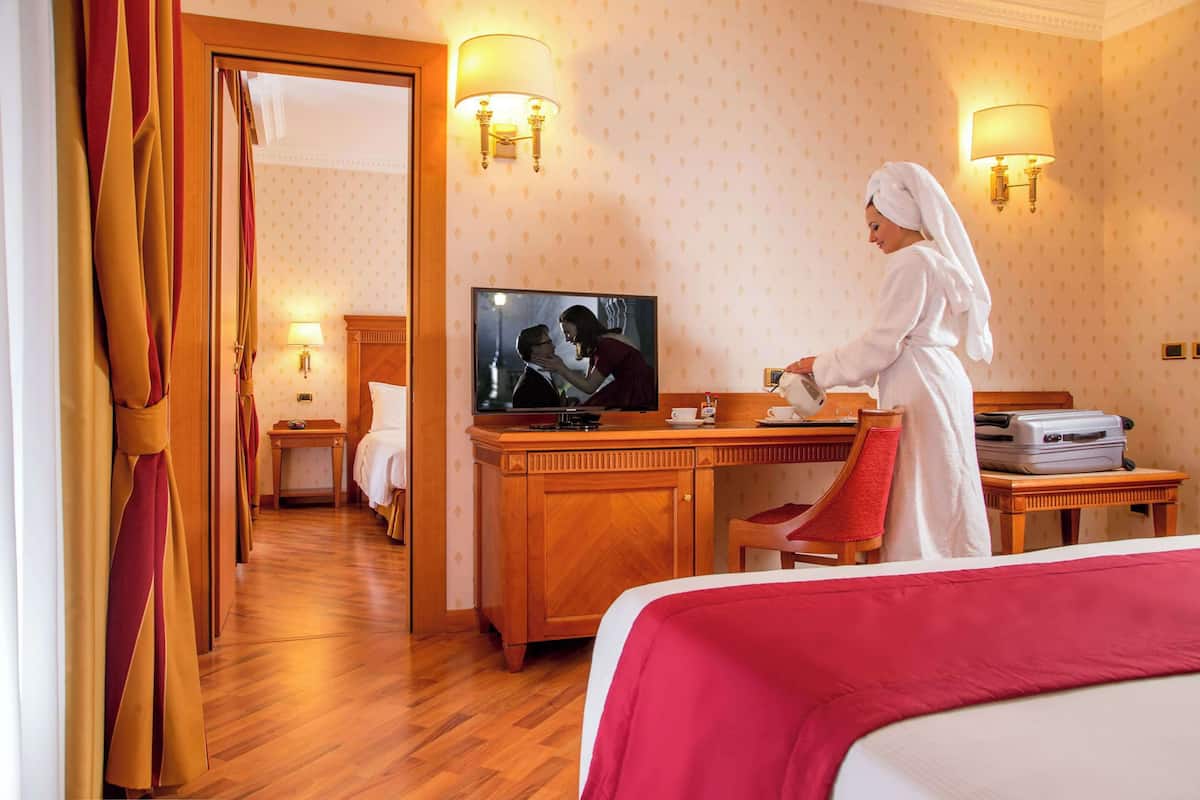 A hotel room with a wooden desk, a television, a bed with a red blanket, and a red chair.