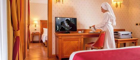 Una habitación de hotel con un escritorio de madera, un televisor, una cama con una manta roja y una silla roja.
