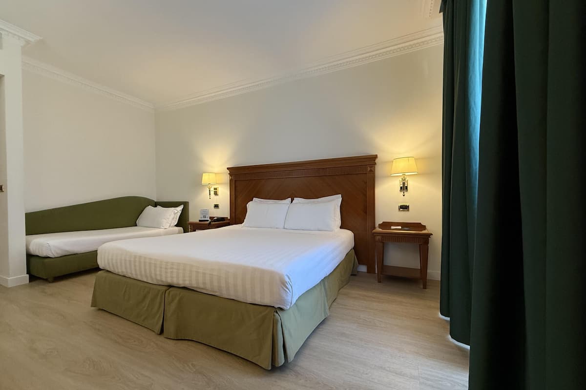 A hotel room with a large bed, a smaller bed, two bedside tables, and a nightstand.