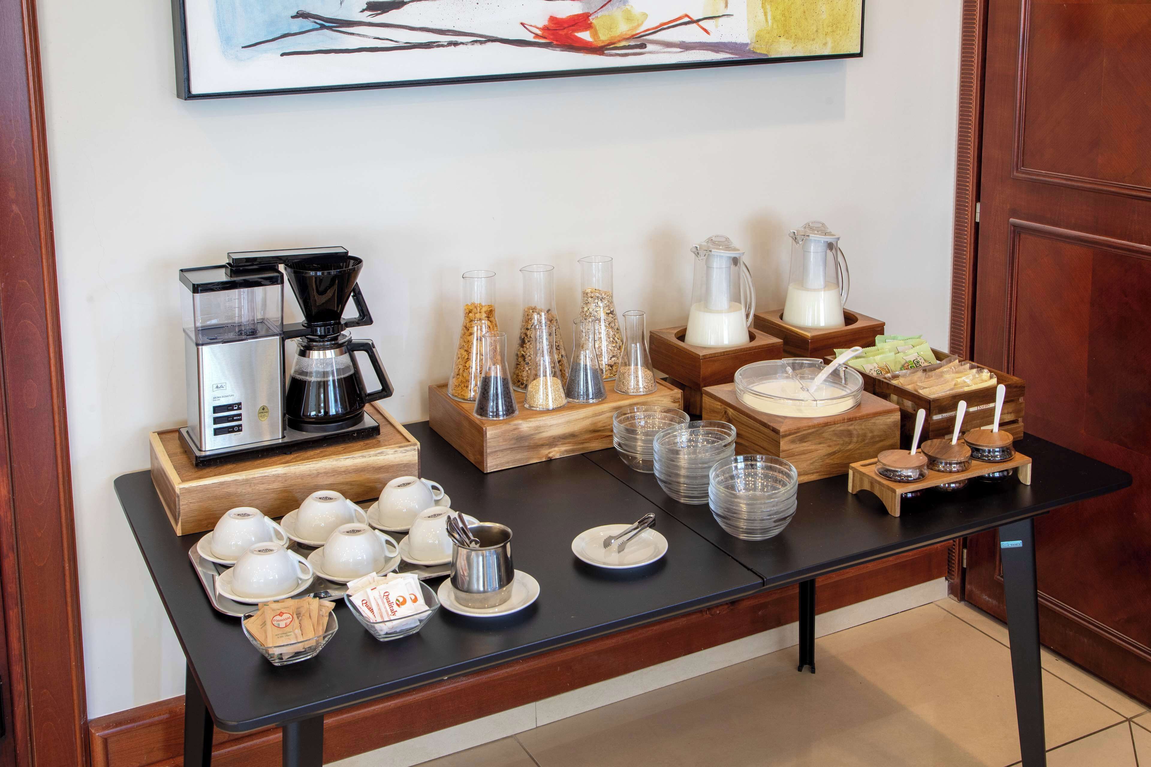 A breakfast buffet setup with coffee machines, glass containers, and serving dishes.