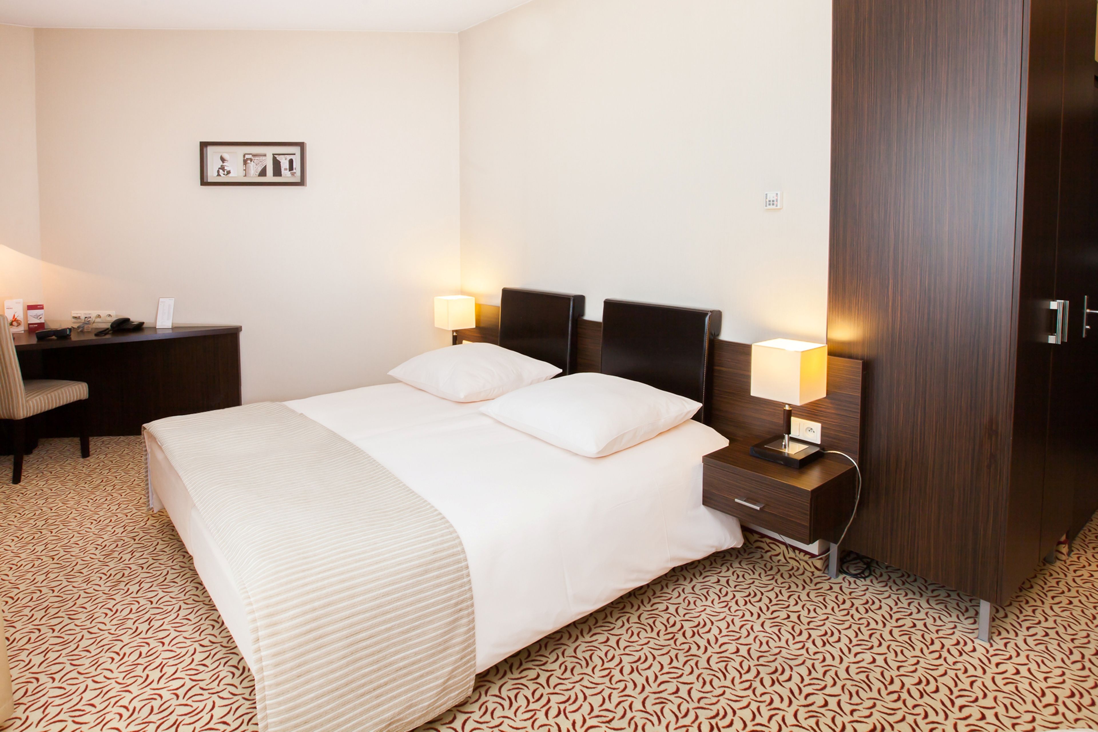 Habitació d'hotel amb un llit gran, dues taules de nit amb làmpades, un escriptori i un armari.