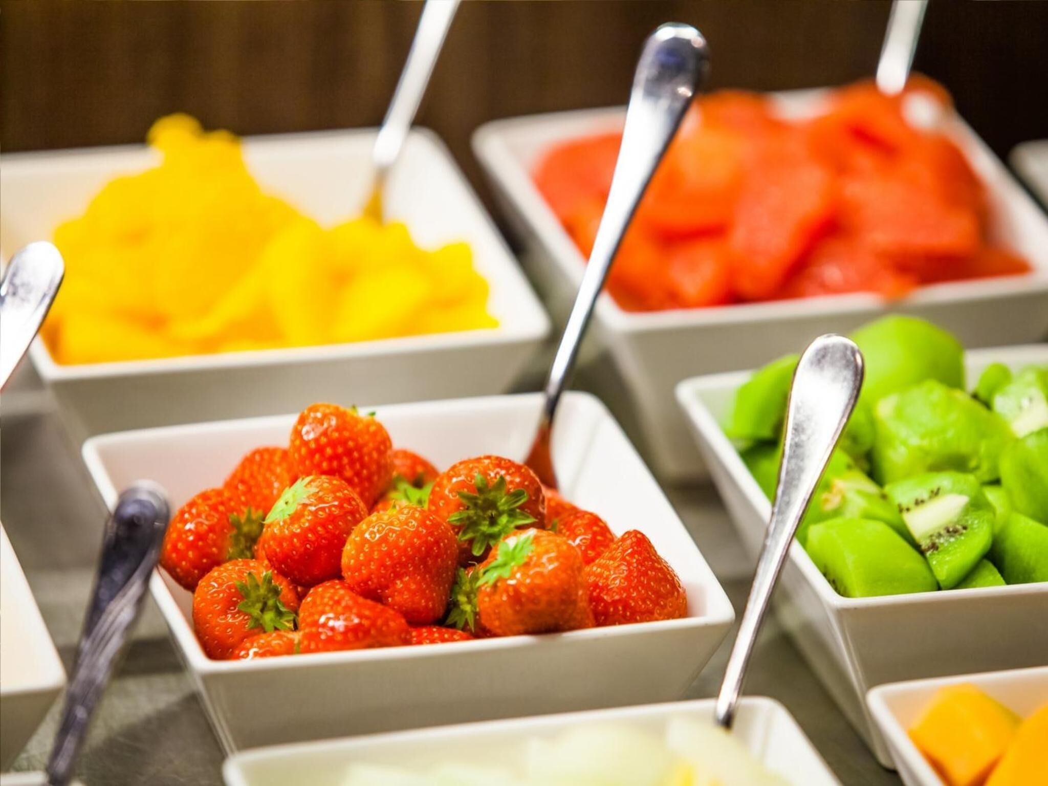 Un bufé con diversas frutas, incluyendo fresas, mangos, sandía y kiwi.