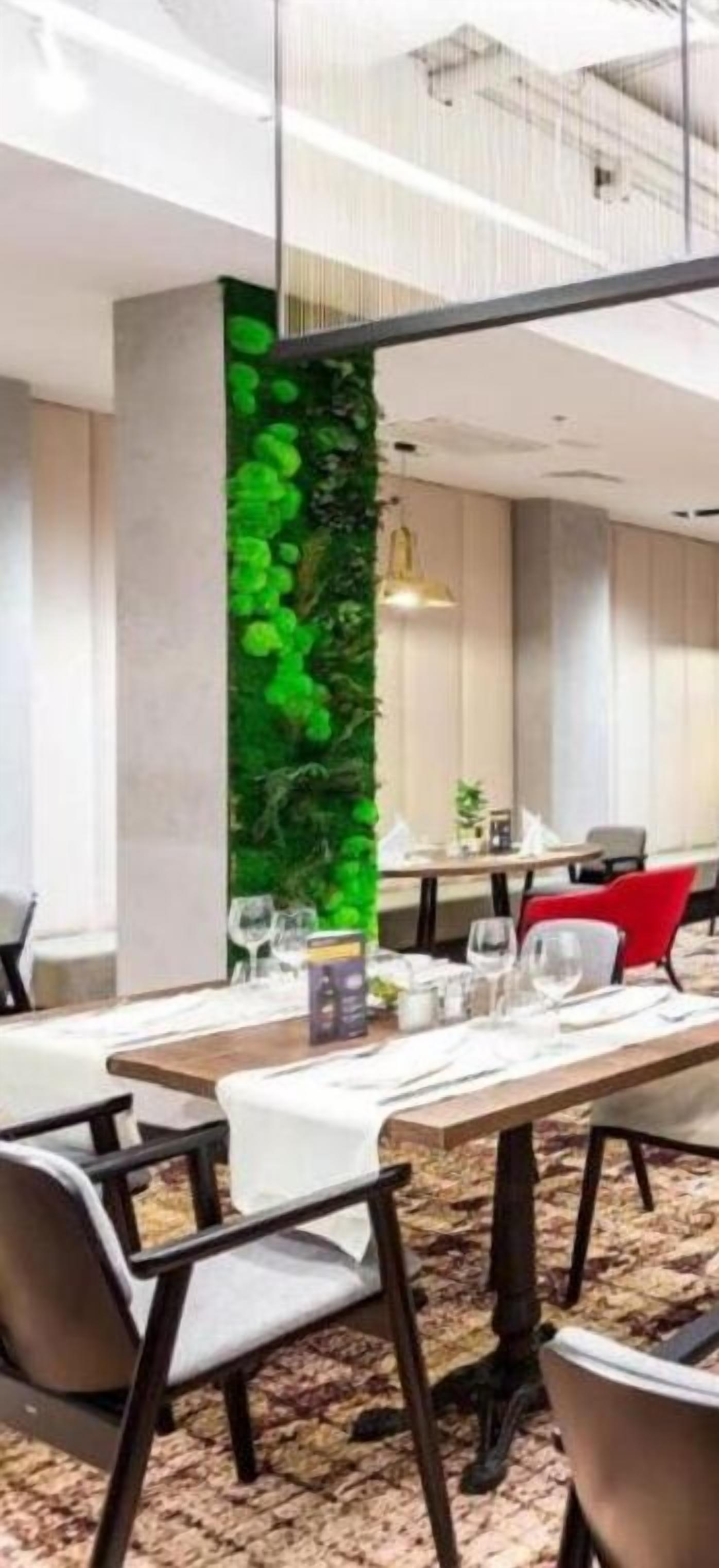 A dining area with a long table set for four, surrounded by chairs. A vertical garden feature is visible on the wall behind the table.