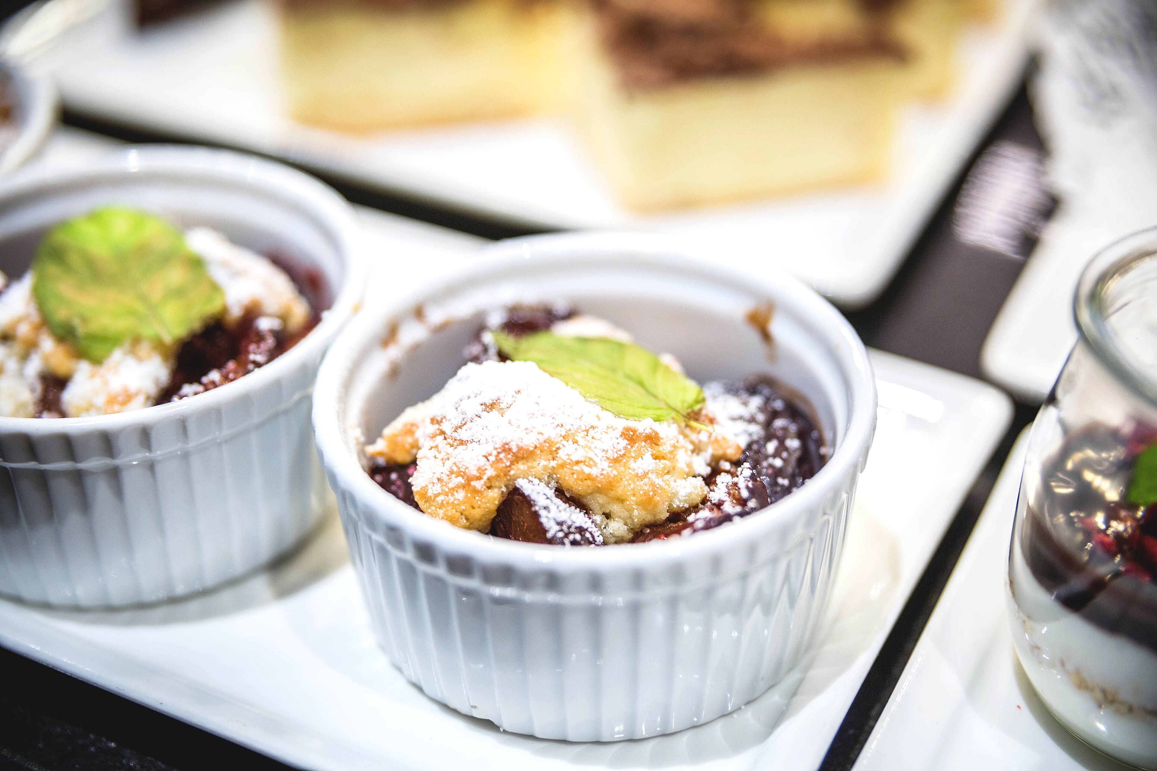 Two white ramekins with dessert on a white plate.
