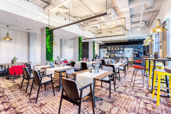 A modern dining area with tables and chairs, a bar area, and a green vertical garden wall. - Qubus Hotel Lodz (Lodz)