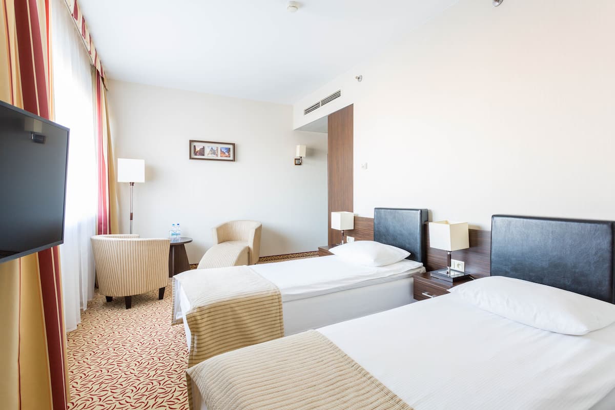 A hotel room with two beds, a TV, a desk with a lamp, and a chair.