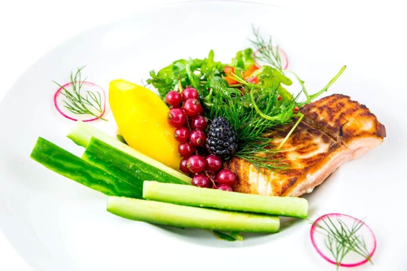 A plate with grilled fish, lemon, radishes, and greens.