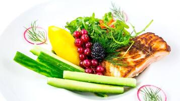 A plate with grilled fish, lemon, radishes, and greens.