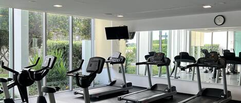 A gym with stationary bikes, treadmills, and a large window providing a view of greenery.