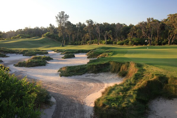 A golf course with sand bunkers, a flag, and a flagpole. - Pullman Magenta Shores Resort (Magenta Shores)