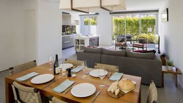 A modern dining area with a wooden table set for four, a grey sofa, and a kitchen in the background.