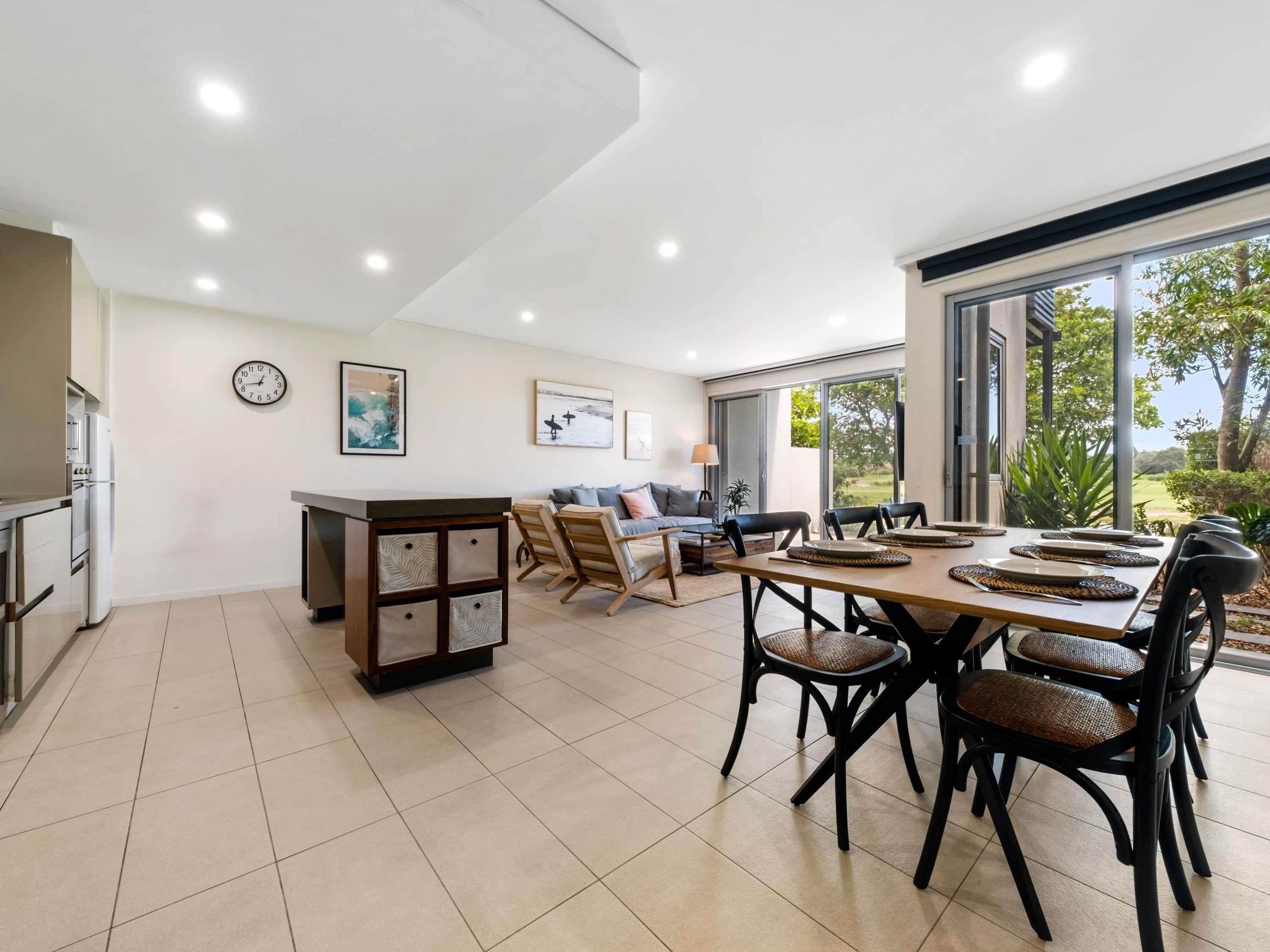 A spacious living area with a dining table, chairs, a sofa, and a kitchen area with a refrigerator and cabinets.