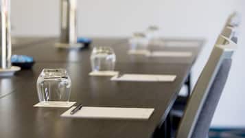 Mesa de conferência com copos de vidro transparentes e canetas, sobre um fundo neutro.