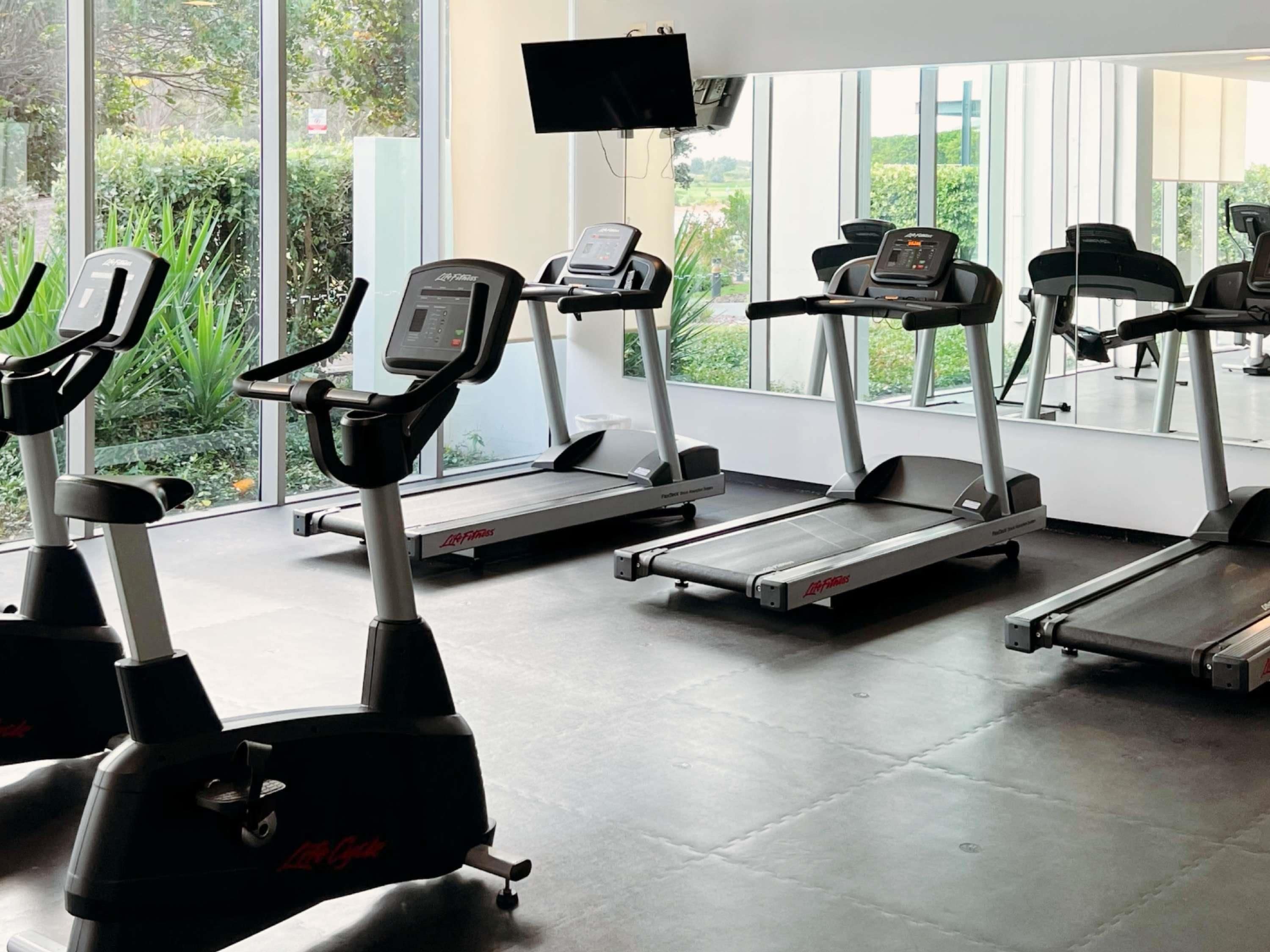 A gym with treadmills, exercise bikes, and a TV screen.