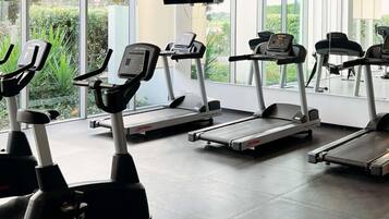 A gym with treadmills, exercise bikes, and a TV screen.