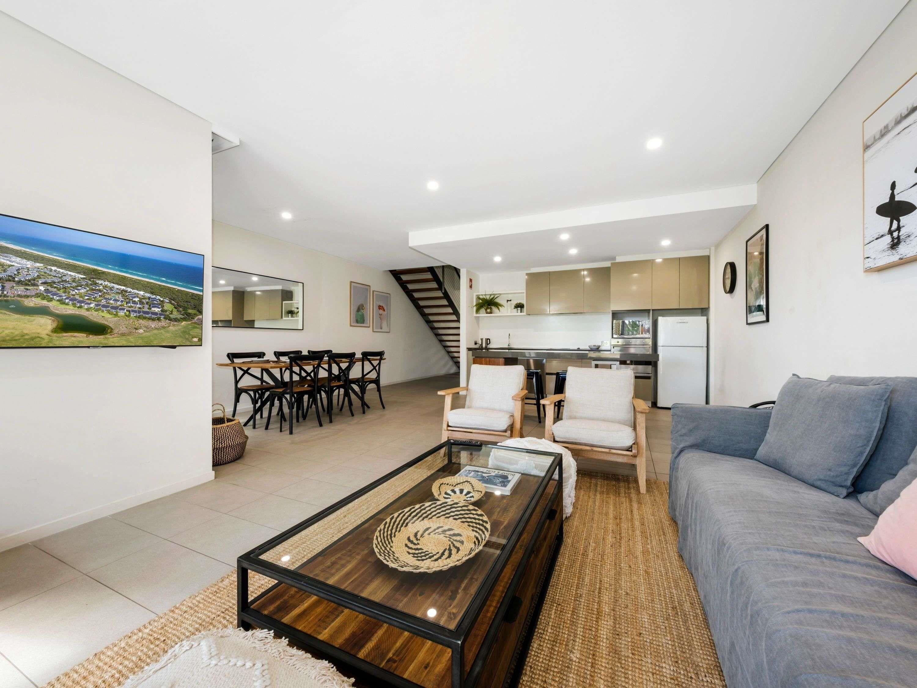 A modern living room with a glass coffee table, a sofa, and a dining area with chairs.