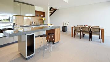 A modern kitchen with a central island, bar stools, a dining area with wooden chairs, and a large potted plant.
