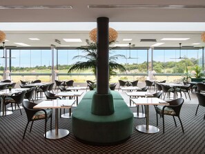 Ein Restaurant mit einer großen zentralen Säule, Tischen, Stühlen und großen Fenstern mit Blick auf einen Golfplatz.