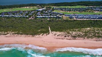 Vista aérea de uma área costeira com praia, campo de golfe e um complexo residencial de arquitetura moderna.