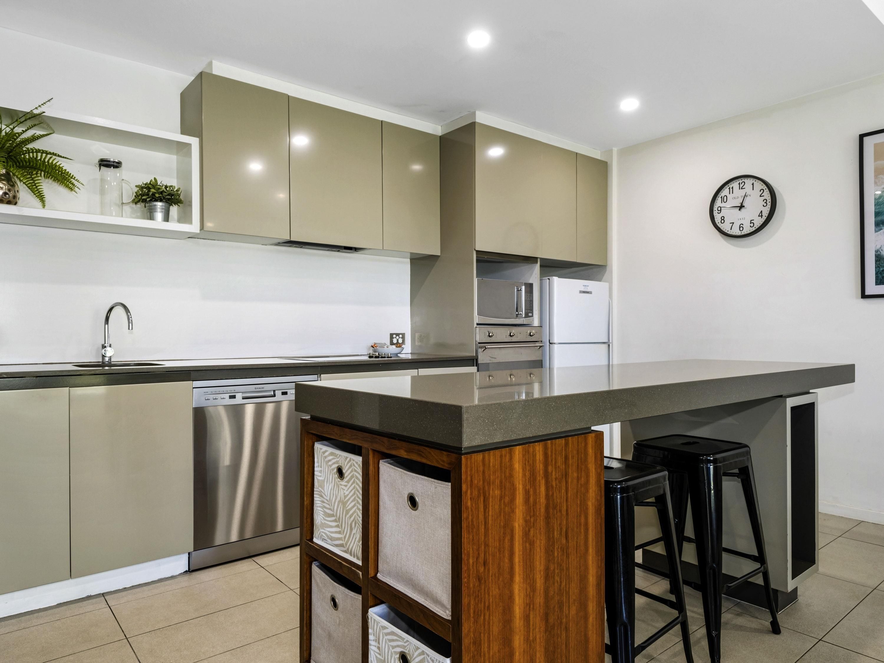 Een moderne keuken met een centraal eiland, roestvrijstalen apparatuur en een klok aan de muur.